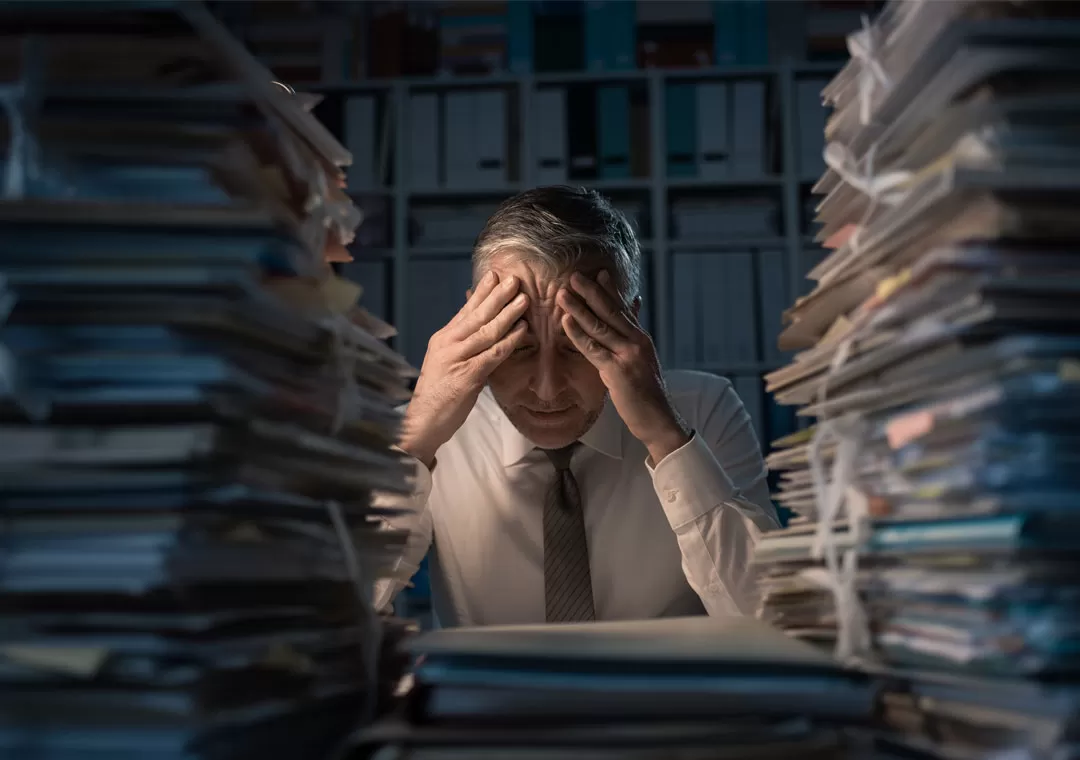 content moderation agents with a headache surrounded by piles of paper in the dark BPO office