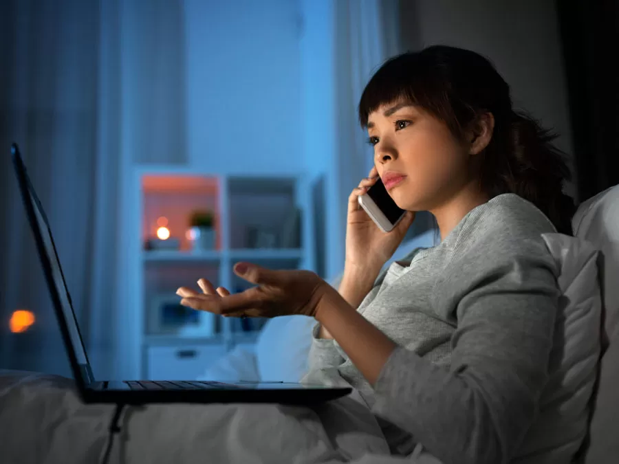 woman speaking to japanese call center agents on phone looking at laptop in bed