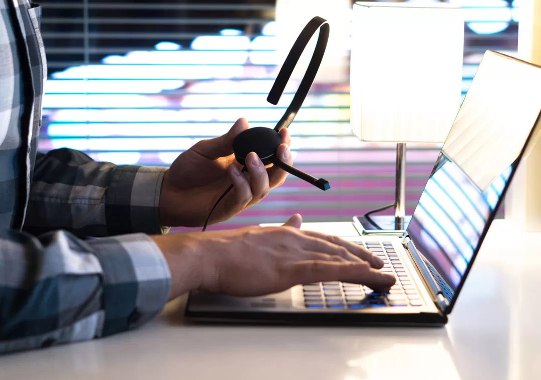 tech support outsourcing agent hands holding call center headset by laptop