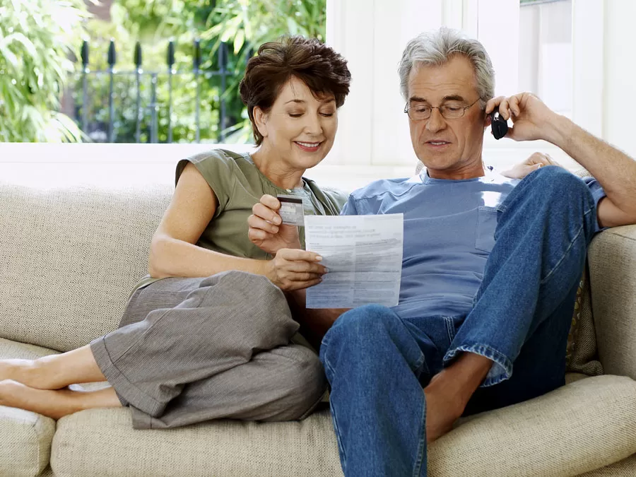 baby boomers elderly couple on couch using phone looking at catalogue
