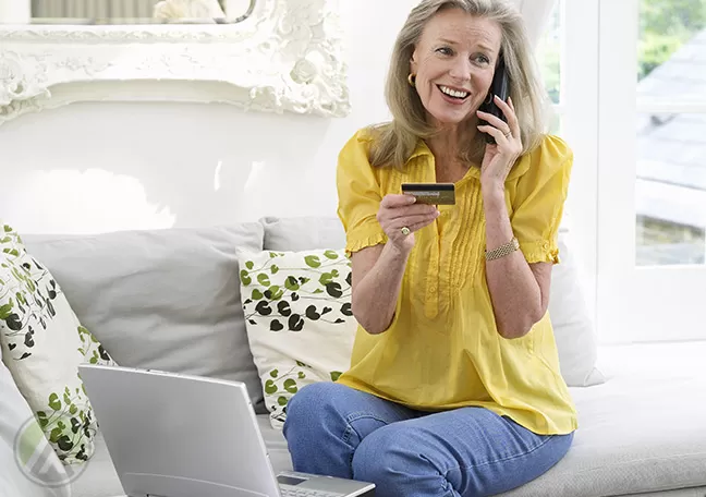 elderly-woman-on-the-phone-holding-a-credit-card-and-facing-a-laptop