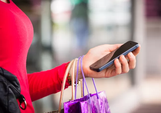 female-millennial-holding-smartphone-shopping-bags