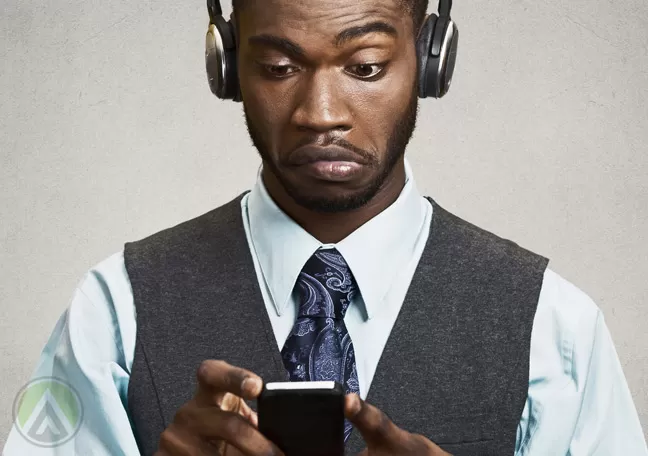 confused-African-American-businessman-in-black-wearing-headphones-looking-at-smartphone