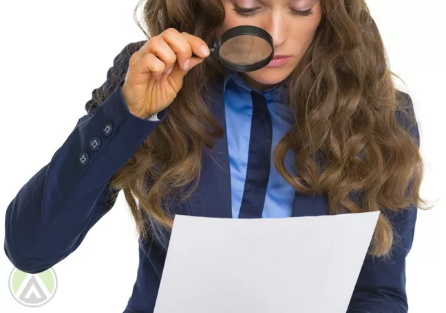 female-employee-in-blue-looking-closely-at-document-with-magnifying-lens