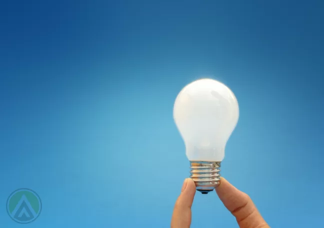 fingers-holding-a-lit-lightbulb-amid-blue-background