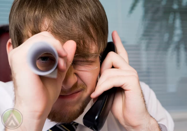 silly-young-male-business-manager-millennial-in-office-looking-through-paper-telescope-while-on-phone-call