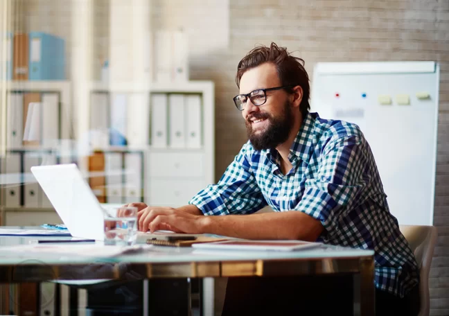 bearded man using laptop in office lounge