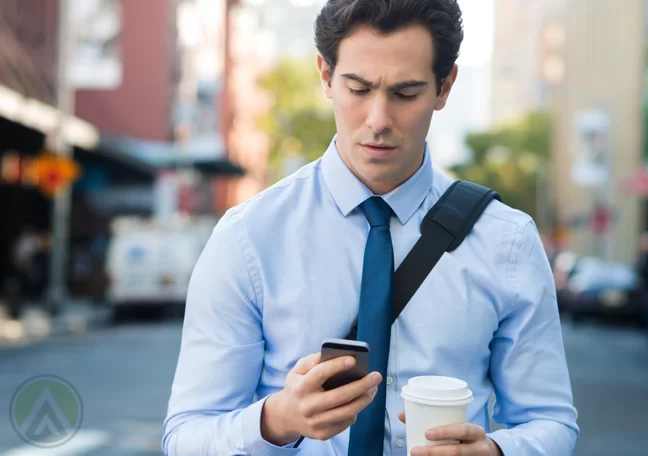 businessman walking street holding cup looking smartphone