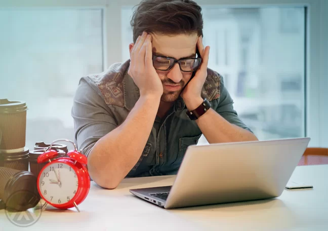 office worker with headache using laptop with red alarm clock coffee cups