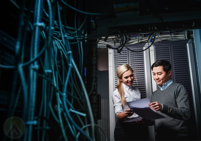 Asian IT manager with system administrator looking at printed reports by IT server room 
