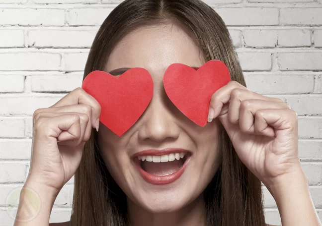 delighted woman holding paper hearts to eyes