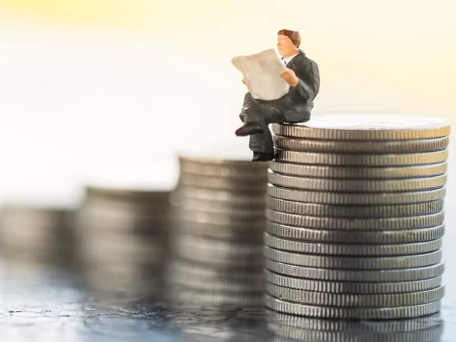 miniature executive reading newspaper on stack of coins showing business progress