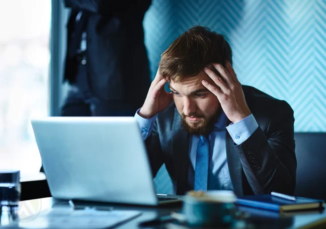 worried businessman with headache in office looking at laptop