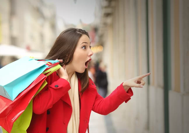 excited shopper carrying shopping bag pointing at shop window display