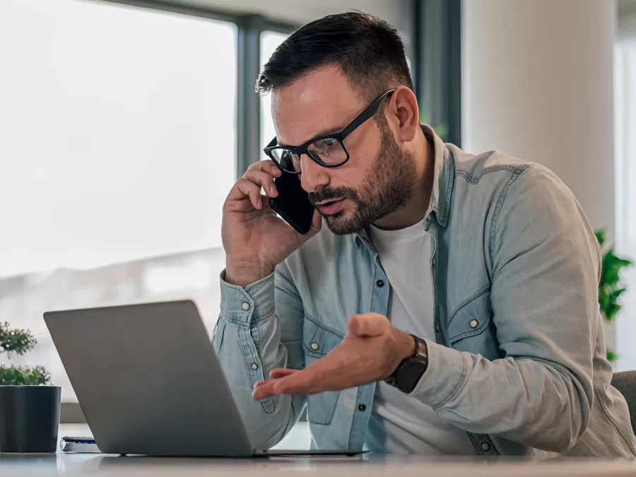 frustrated man calling customer service pointing to laptop